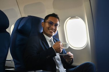 Positive businessman passenger drinking coffee from paper cup while sitting comfortable seat in airplane cabin.