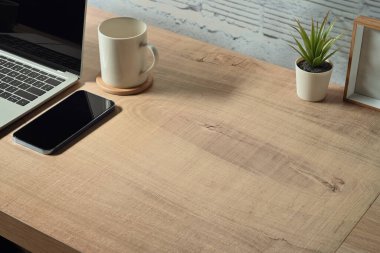 Simple workplace with smart phone, laptop and cup of coffee on wooden table. Copy space for your text.
