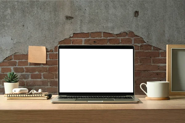 Modern industrial creative workspace with laptop computer, coffee cup, stationery and picture frame on wooden table.