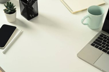 Top view of white office desk with smart phone, laptop computer, coffee cup and supplies. Copy space for text.