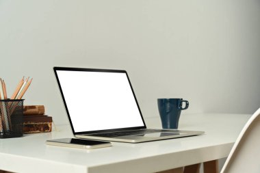 Laptop computer with blank screen, tablet, books and cup of coffee on white table.