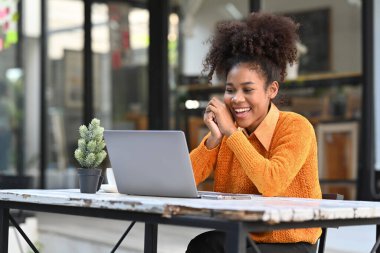 Cheerful African American woman having a video call or watching online webinar on laptop while sitting in outdoor cafe.