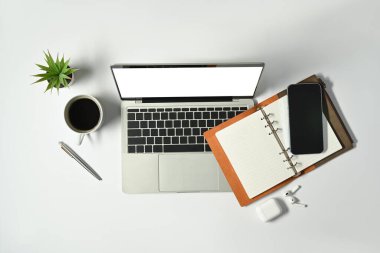White office desk with laptop, notepad, mobile phone and coffee cup. Top view modern workplace.