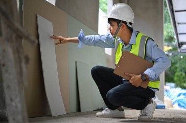 Young asian man inspectors holding clipboard and checking building material at construction site. 