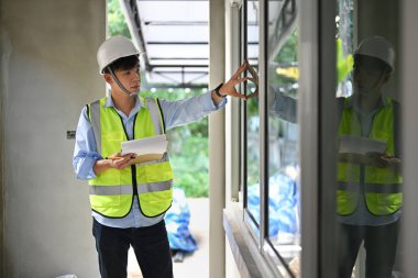 Asian man inspector in safety helmet and vest holding clipboard inspecting the reconstructed construction.