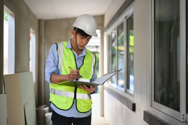 Engineer man looking at blueprints and checking building construction progress, working at construction site.