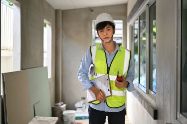 Portrait of engineer man in safety helmet and reflective vest standing in construction site and looking at camera.