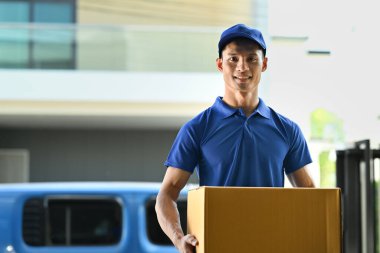 Portrait of delivery man carrying cardboard parcel and smiling at camera. Delivery service, post and shipping concept.