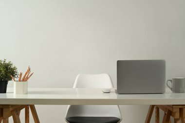 Modern home office interior with laptop computer, pencil holder, coffee cup and potted plant on white table.