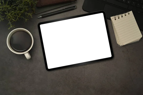 Digital tablet with blank display, cup of coffee and notepad on black slate texture background.