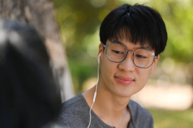 Image of young couple reading a book and listening to music in earphones while relaxing at public park together.