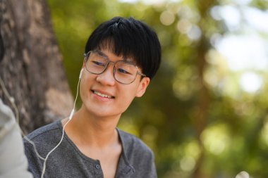 Image of young couple reading a book and listening to music in earphones while relaxing at public park together.