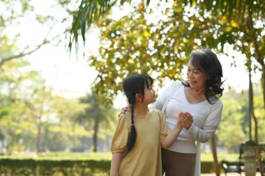 Loving mature grandmother and smiling little grandchild walking, enjoying spending time together in summer park.
