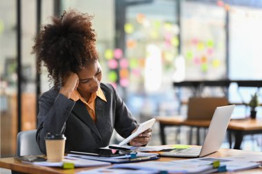 Stressed female accountant working with financial document and using calculator at her office desk.