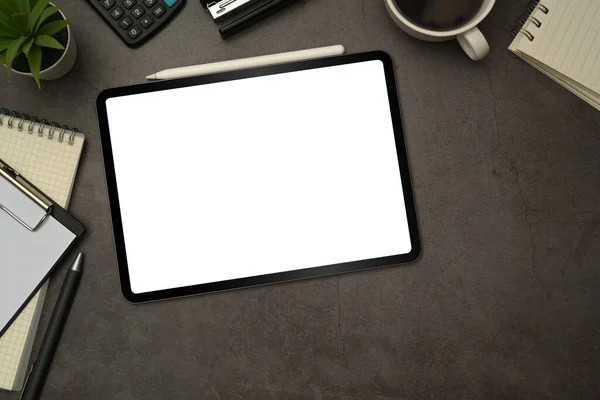 Top view of digital tablet with blank screen, cup of coffee and notepad on black slate texture background.