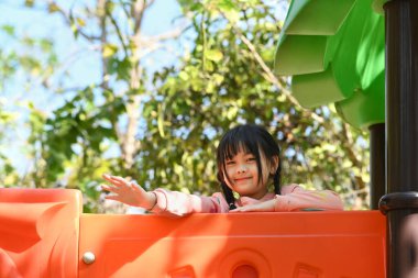Banliyö evinin avlusunda oyun parkında eğlenen aşırı neşeli küçük kız. Eğlence parkının çocukluk ve ekipmanları.