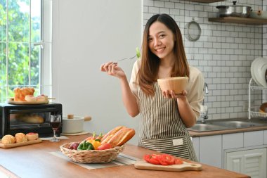 Modern mutfakta taze salata yiyen güzel genç bir kadının portresi. Refah ve sağlıklı yaşam tarzı kavramı.