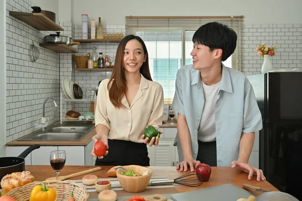Mutfakta sağlıklı yemek pişirirken sohbet eden mutlu genç bir çiftin görüntüsü..
