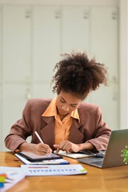 Odaklanmış kadın muhasebeci mali belgelerle çalışıyor ve ofiste dijital tablet kullanıyor.