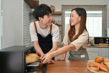 Fransız ekmeğini fırından çıkaran mutlu çift modern mutfakta birlikte yemek hazırlıyorlar..