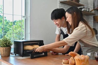 Güzel, genç bir çift fırında ekmek pişiriyor, modern mutfakta birlikte kahvaltı hazırlıyorlar..