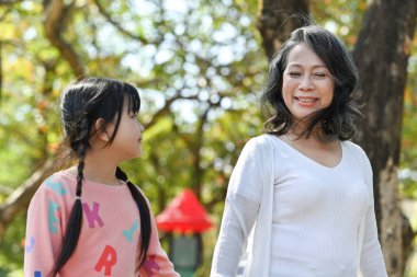 Happy mature grandmother and smiling little grandchild walking, enjoying spending time together in summer park.