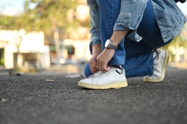 Cropped image of hipster man traveller tying shoe laces for city walk.