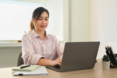 Confident female office worker watching online presentation on laptop computer at modern workplace.