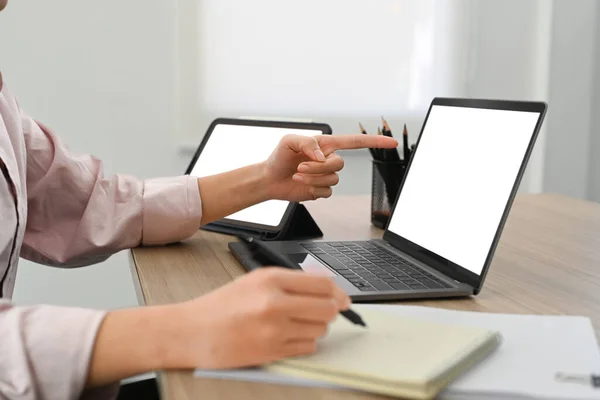 Cropped image of businesswoman pointing on laptop screen and writing on notepad.