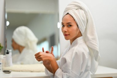 Attractive young woman in bathrobe making daily beauty routine at home. Beauty treatment and self care concept.