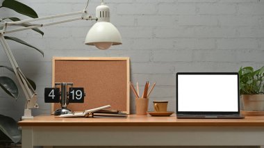 Front view of laptop computer with empty display, lamp, coffee cup and board on wooden desk.