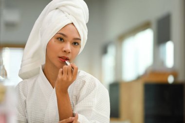 Portrait of attractive young woman applying lipstick and looking in mirror. Daily beauty routine and cosmetics concept.