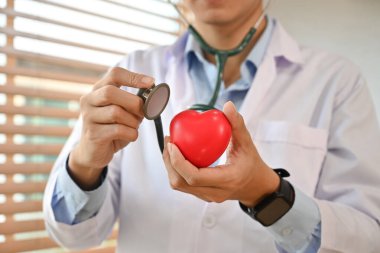 Doctor in white uniform holding stethoscope and red heart shape. Health care, organ donation and cardiology concept.