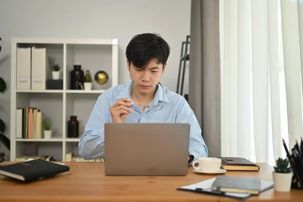 Focused man manager looking at laptop watching online webinar training or having virtual meeting video conference in office.