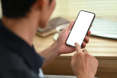 Young man hand checking social media on mobile phone. Over shoulder closeup view, blank screen for graphic display montage.