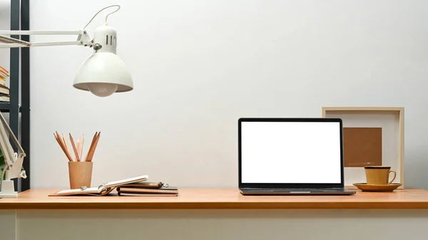 Modern creative workspace with laptop, picture frame and lamp on wooden desk. Blank screen for graphic display montage.