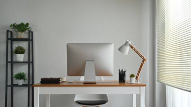 Modern creative workspace with computer monitor and supplies and lamp on wooden working desk.