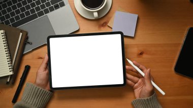 Creative woman hands holding digital tablet with white empty display over wooden working desk.
