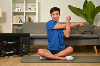 Sporty young asian man stretching his arms before exercises at home. Healthy lifestyle, sport and motivation concept.