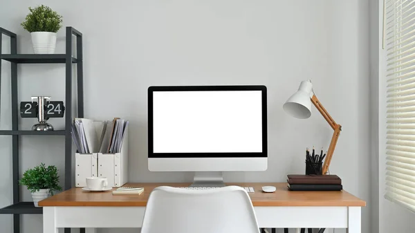 Front view of blank computer screen, lamp and supplies on wooden desk. Empty screen for your creative design.