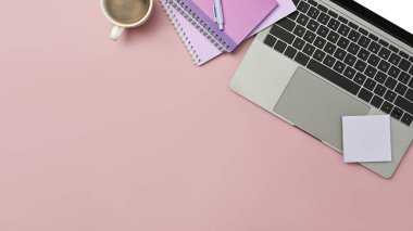 Top view of laptop computer, sticky notes, notebooks and coffee cup on pink background.