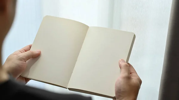 Over shoulder view of hands holding a blank opened notebook. Copy space for your advertise text.