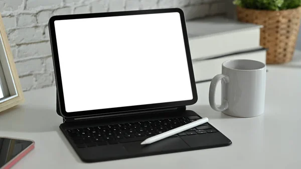 Digital tablet with wireless keyboard, coffee cup and supplies on white working desk. Blank screen for advertise webpage or text.