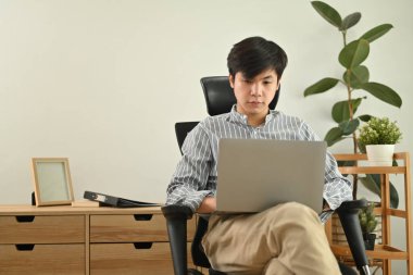Portrait of start up businessman sitting on comfortable office chair in modern workplace and using laptop.