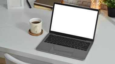 White office desk with laptop computer, cup of coffee and potted plant. Blank display for text information or content.