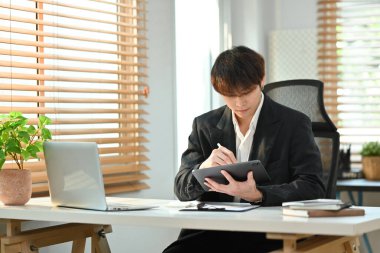Millennial asian man finance manager planning work projects using digital tablet in bright office.