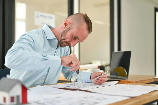 Concentred caucasian architect man working with blueprint, sketching a construction project at his workstation.