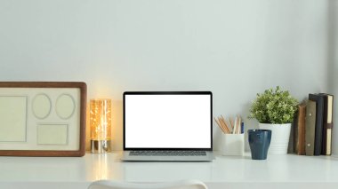 Home office desk with laptop computer, coffee cup, potted plant and picture frame. Empty screen for graphic display montage.