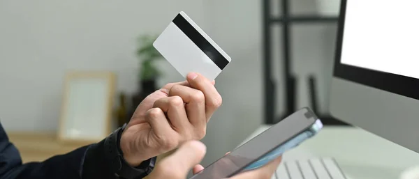 Man holding credit cad and using mobile phone smartphone for online banking transaction or entering data for website form.