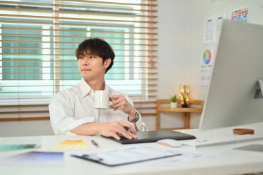 Thoughtful asian man web developer drinking coffee and looking through window, pondering idea in office.